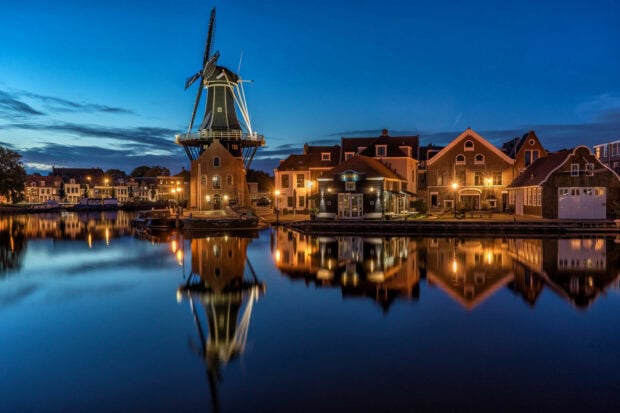 Historic windmill and traditional houses reflected in calm water in Netherlands at dusk