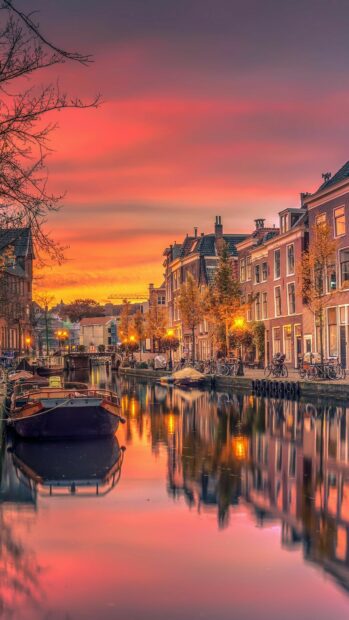 Sunset over a canal in Netherlands cityscape with boats and autumn trees