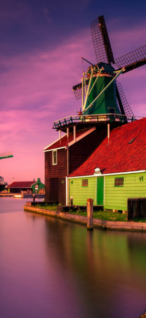 Traditional Dutch windmill and colorful houses along water canal in Netherlands at sunset