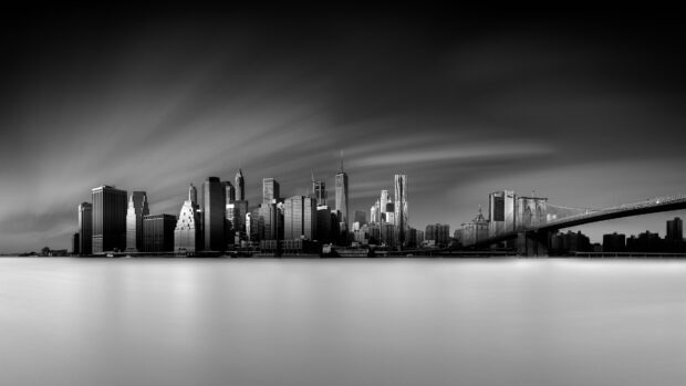 Black and white view of the New York skyline with the Brooklyn Bridge over calm water