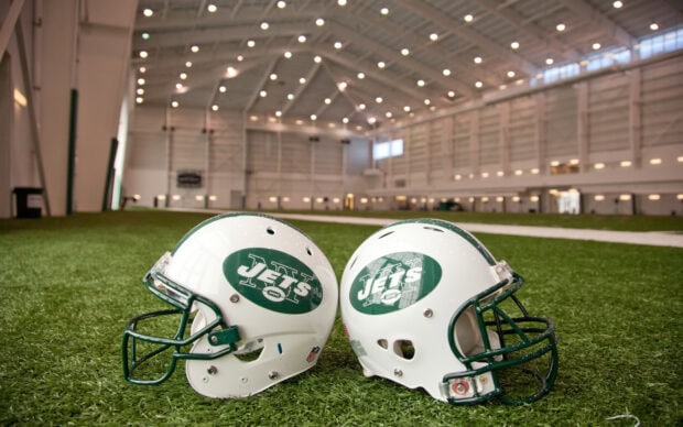 Two New York Jets helmets resting on artificial turf inside an indoor football practice facility
