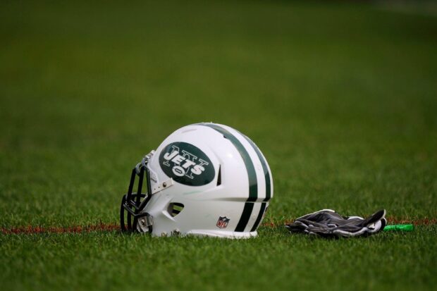 A New York Jets football helmet resting on green grass with gloves beside it