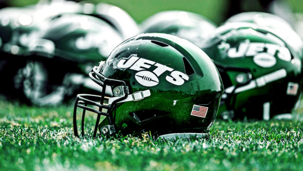 A close up of a New York Jets helmet on grass with other helmets in the background