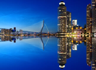 Modern city skyline with illuminated buildings and a bridge at night reflecting on calm water