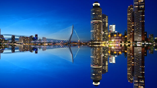 Modern city skyline with illuminated buildings and a bridge at night reflecting on calm water