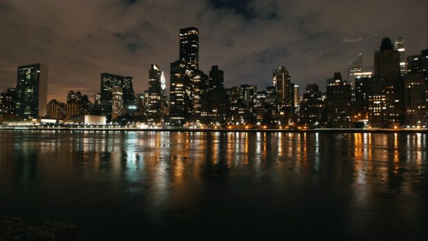 Night skyline of a city reflected in water with illuminated buildings and cloudy sky
