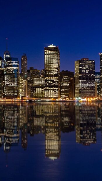 Night skyline with illuminated city buildings reflecting on calm water at dusk