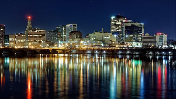 City skyline at night with illuminated buildings and river reflections in a clear sky