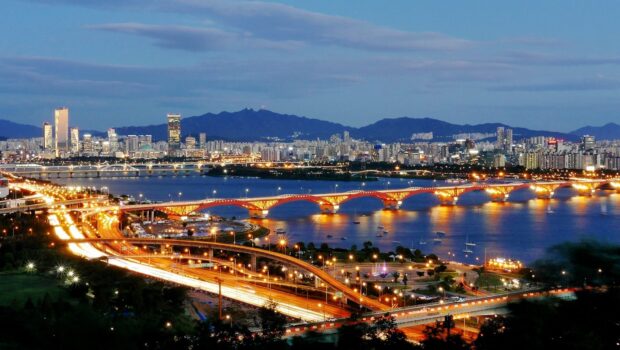A vibrant night skyline with city lights and a bright bridge over the river