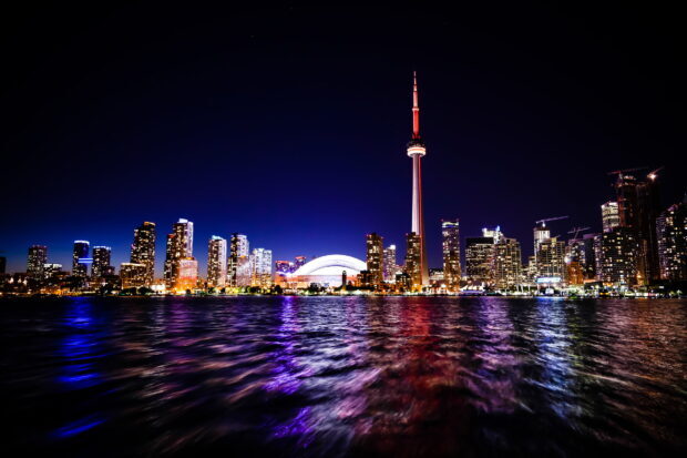 Toronto city skyline at night with illuminated buildings and a tall tower reflected on water