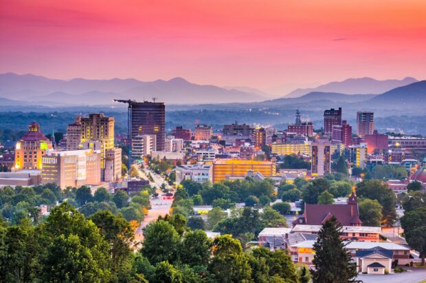A vibrant cityscape of North Carolina with mountain ranges under a colorful sunset sky