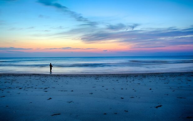 A person fishing at the beach during sunset in North Carolina with calm waves and colorful sky