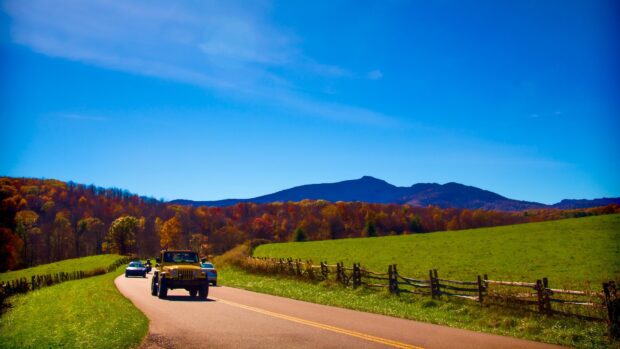 A scenic North Carolina landscape with a green field and vehicles driving on a rural road