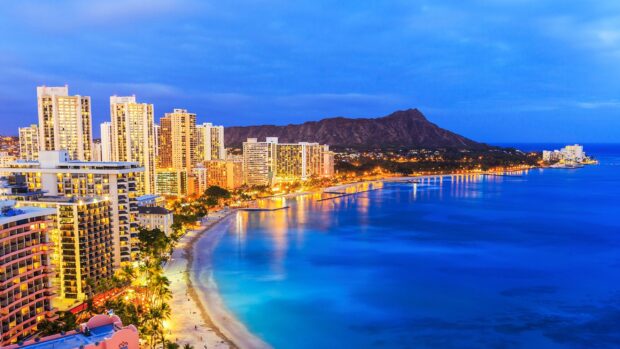 The vibrant cityscape of Oahu at dusk with illuminated buildings and the ocean shoreline