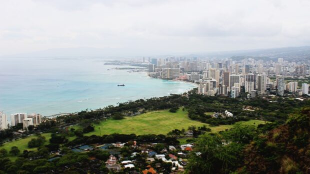 Aerial view of Oahu cityscape and coastline with clear ocean and green parks