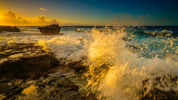 Golden sunset lighting crashing waves on rocky shores of Oahu coastline