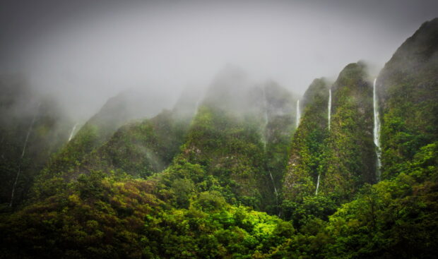Misty mountains covered with lush vegetation on Oahu with multiple waterfalls visible