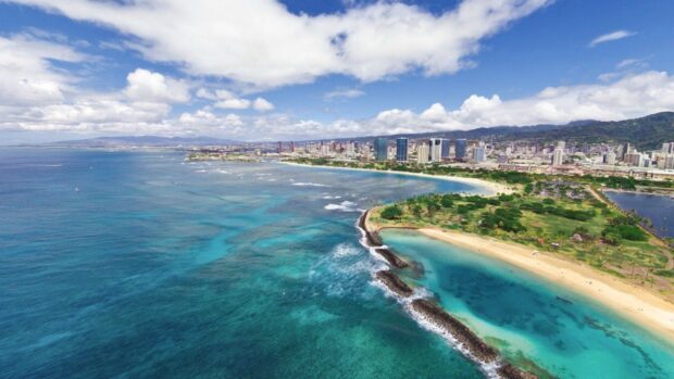 Aerial view of Oahu coastline with clear turquoise water and city skyline in the background