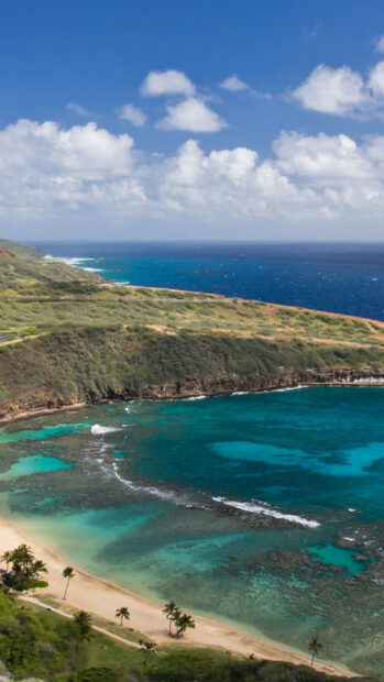 A beautiful scenic view of Oahu coastline with clear turquoise water and green hills under a blue sky