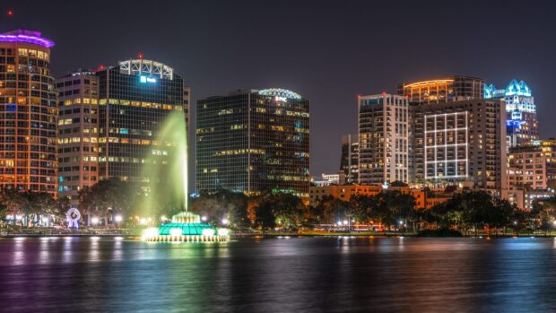 Night view of Orlando city skyline with lit fountain and high rise buildings reflecting on water