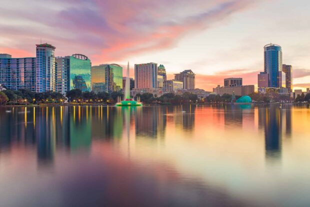 Orlando city skyline with green lit fountain reflecting on the lake at sunset