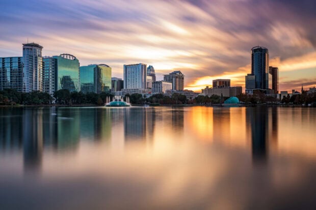 Orlando skyline reflecting on the calm lake during a vibrant sunset with clear skies and city buildings