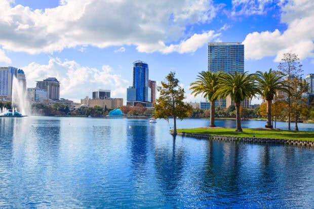 Orlando skyline with tall buildings and palm trees reflected in the lake under a blue sky