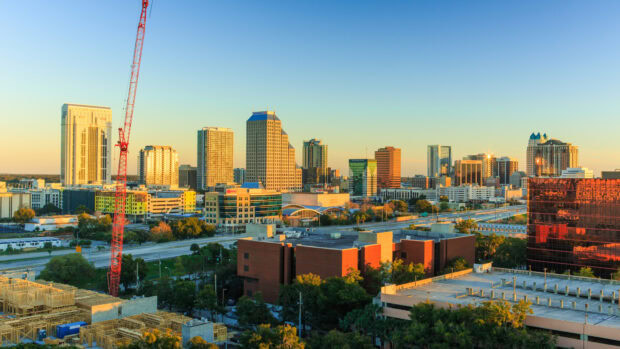 The Orlando skyline features tall buildings and a bright red crane during golden hour