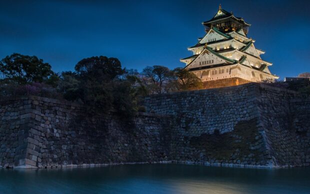 Illuminated Osaka Castle surrounded by stone walls and water at dusk with clear sky