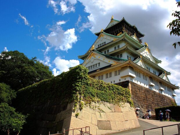 Osaka Castle surrounded by stone walls and greenery under a bright blue sky with white clouds