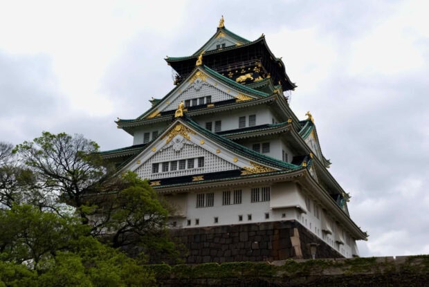 A detailed view of Osaka Castle architecture with green rooftops and golden decorations surrounded by trees