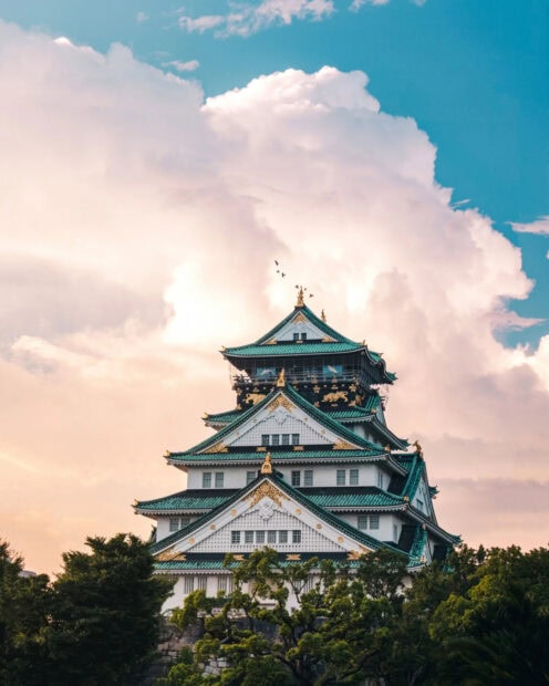 A stunning view of Osaka Castle surrounded by trees under a cloudy sky