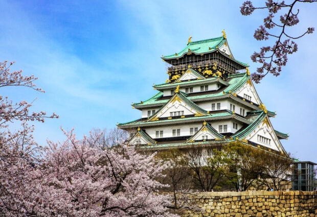Osaka Castle surrounded by blooming cherry blossoms under a clear blue sky