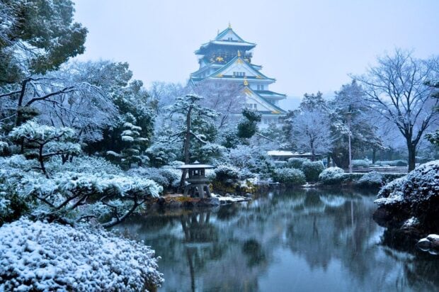Osaka Castle surrounded by snowy trees and a calm pond during winter in Japan