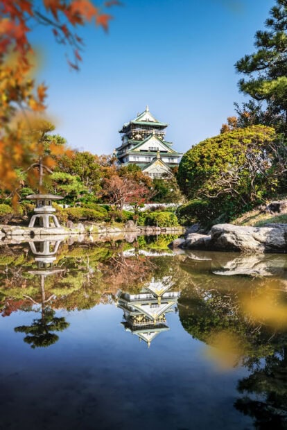 Beautiful Osaka Castle surrounded by autumn trees reflected in a serene pond