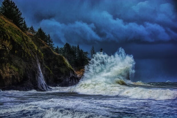 Rough Pacific Ocean waves crashing against rocky cliffs with a lighthouse on a stormy day