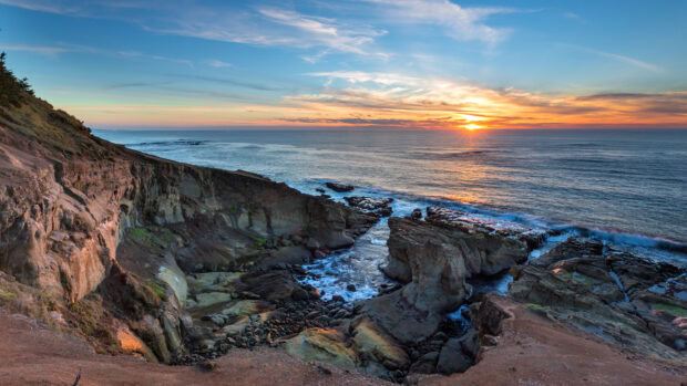 Rocky cliffs and calm Pacific Ocean at sunset with clear sky and gentle waves