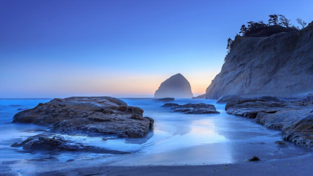 Rocky coastline with calm waters and a large sea stack in the Pacific Ocean at sunset