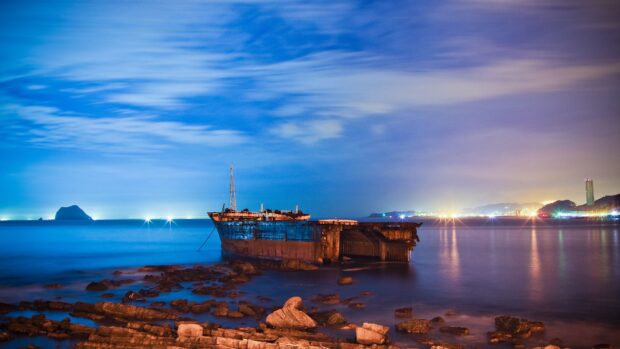 Rusty shipwreck on the Pacific Ocean coast surrounded by rocks and city lights