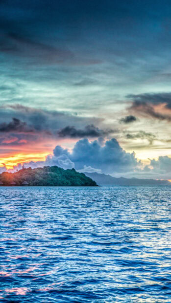 Pacific Ocean with island and colorful sunset clouds over the horizon