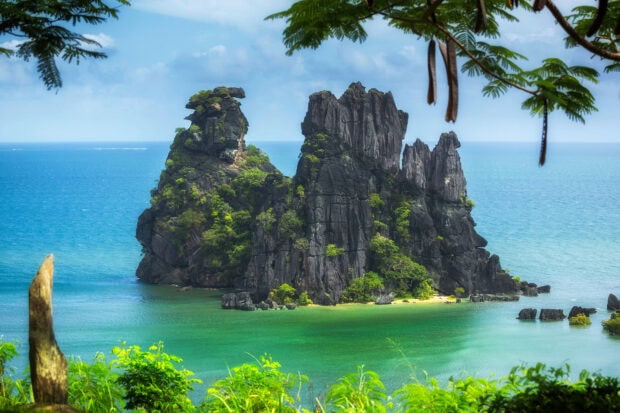 A rocky island with lush greenery surrounded by the Pacific Ocean in clear blue water