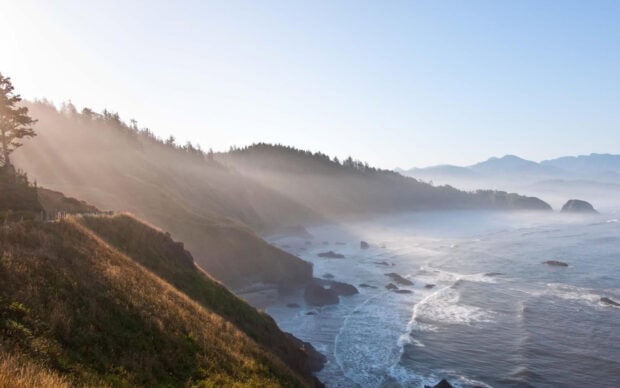 Morning sun rays shine over Pacific coastline cliffs and ocean waves