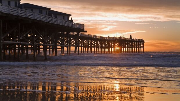 A wooden pier over the Pacific Ocean with a sunset sky and waves crashing on the shore