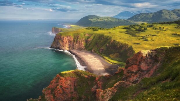 A breathtaking view of rugged cliffs and green hills along the Pacific Ocean coastline