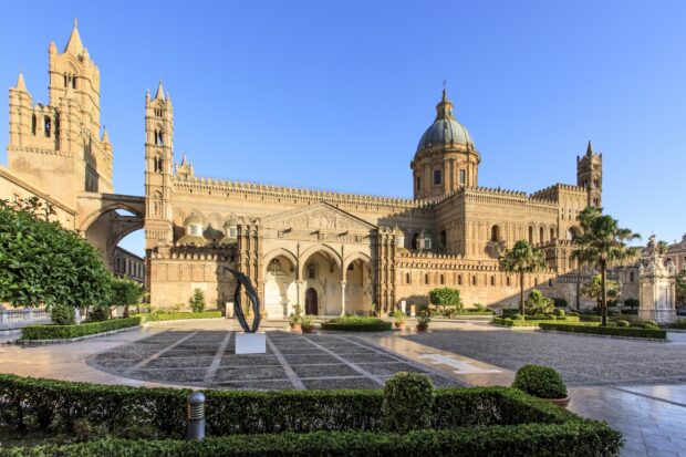 Historic Palermo cathedral with clear blue sky and manicured garden in foreground