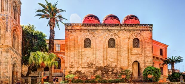 Historic Palermo building with three red domes and palm trees in a sunny sky