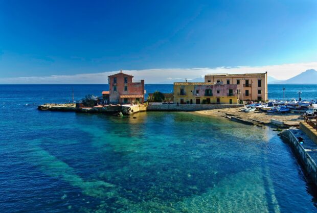 Old buildings by the clear sea in Palermo with bright blue sky and boats