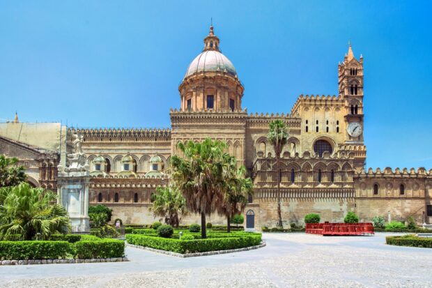 The historic Palermo cathedral with a large dome and garden under a clear blue sky