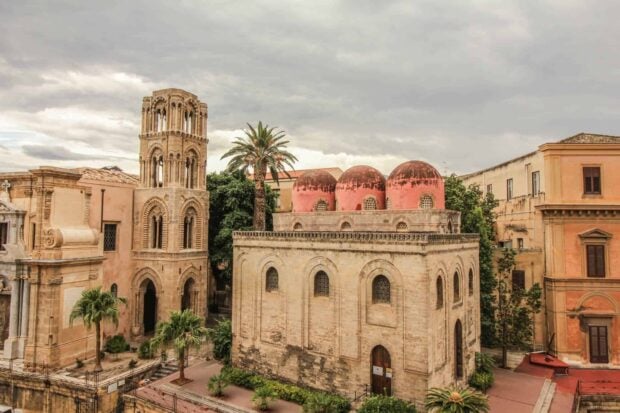 Historic Palermo architecture featuring red domes and stone buildings under cloudy sky