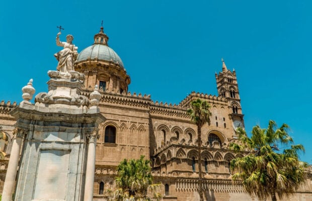 Historic Palermo architecture with statue and palm trees under clear blue sky